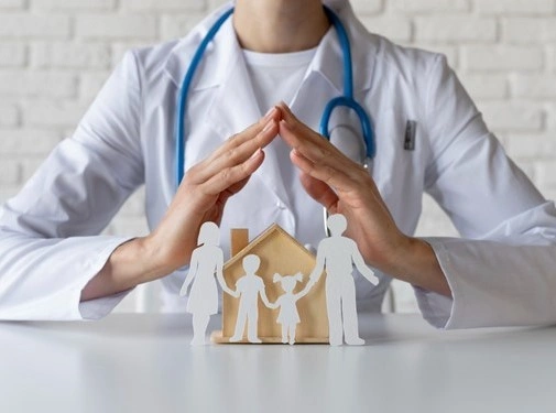 Doctor protecting paper family cutout house with hands